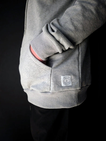 side view of the purpose hoodie by advocäte showing kangaroo pocket, ribbed cuff, and woven brand patch in organic cotton fleece